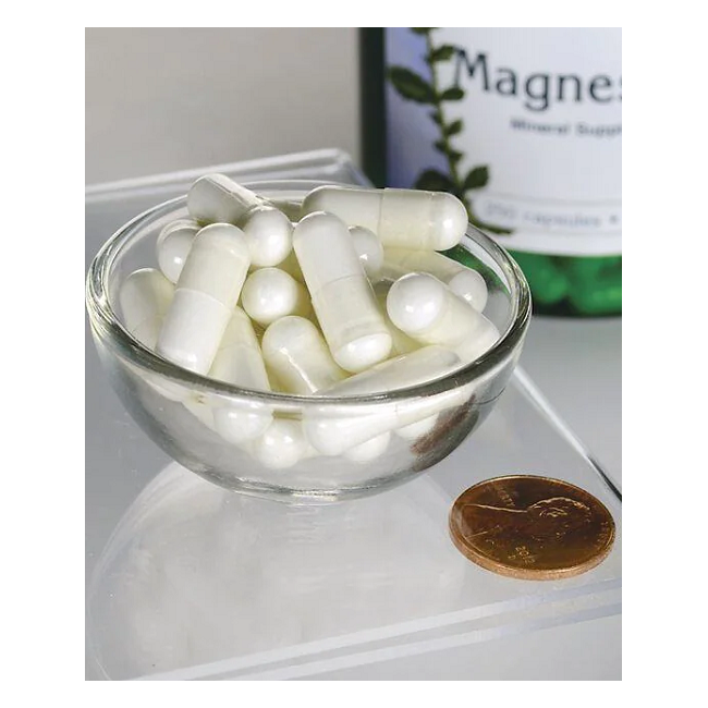 A clear bowl with white capsules from Swanson's Magnesium Oxide 200 mg (250 Capsules) sits next to a penny and a labeled bottle, emphasizing its role in bone health on the transparent surface.