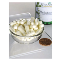 Thumbnail for A small glass bowl of white capsules sits next to a US penny on a clear surface. In the background, a partially visible Swanson bottle reads 