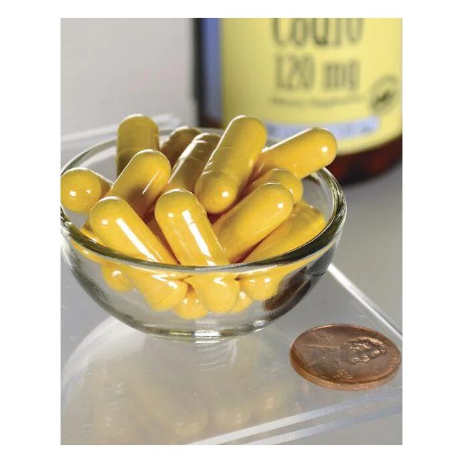 A small glass bowl with several yellow capsules, identified as Swanson Coenzyme Q10 120 mg 100 Capsules, lies next to a penny with a blurred medicine bottle in the background.