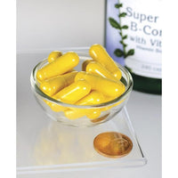 Miniatura de Swanson B-Complex com cápsulas de vitamina C numa taça ao lado de uma moeda.