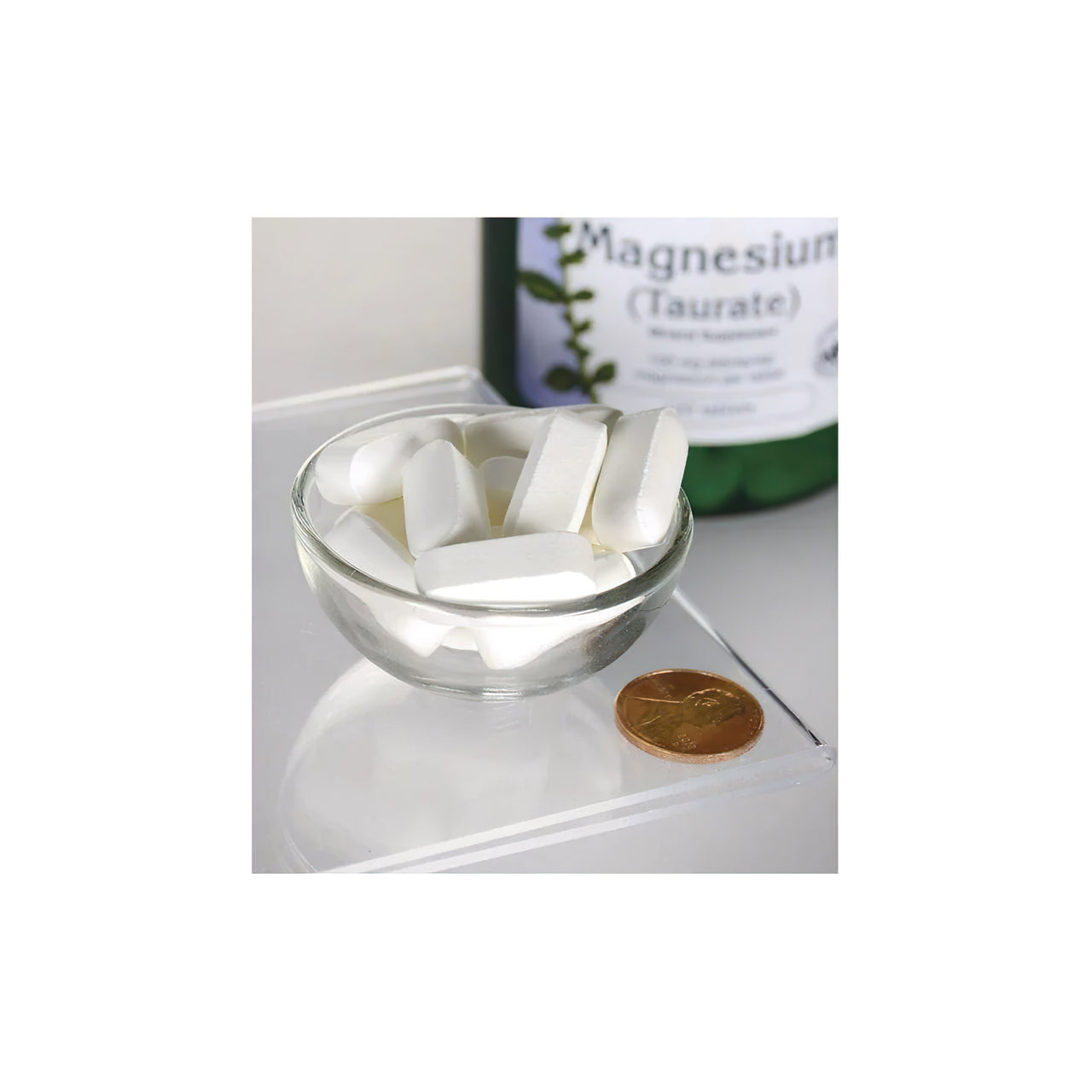 Um frasco de Swanson Magnesium Taurate 100 mg 120 tab sentado ao lado de uma tigela de comprimidos brancos.