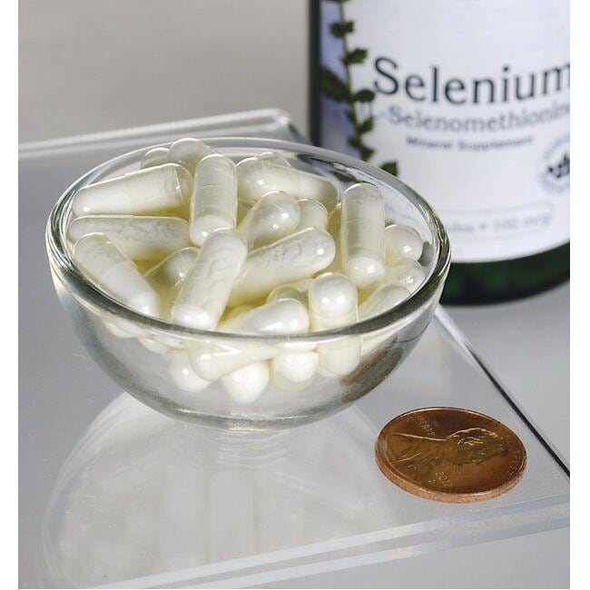 Swanson Selénio - 100 mcg 200 cápsulas L-Selenometionina numa tigela ao lado de uma moeda, oferecendo apoio antioxidante para a saúde cardiovascular.