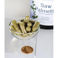 Miniatura de Swanson Saw Palmetto - 540 mg 250 cápsulas, conhecidas pelo seu papel na promoção da saúde da próstata e do fluxo do trato urinário, são apresentadas numa tigela ao lado de uma moeda.