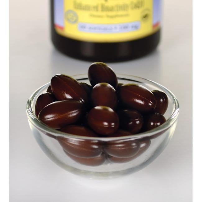 A small glass bowl filled with brown capsule-shaped supplements, designed for cardiovascular health, with a partially visible Swanson Ubiquinol 100 mg 60 Softgels supplement bottle in the background.